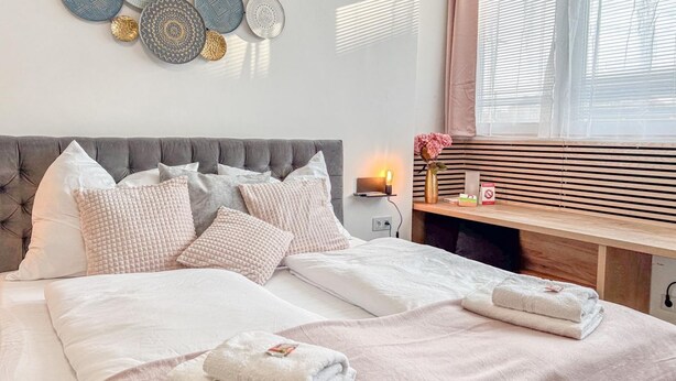 Una cama bien hecha con almohadas, una mesita de noche con lámpara y una pared decorada con platos.