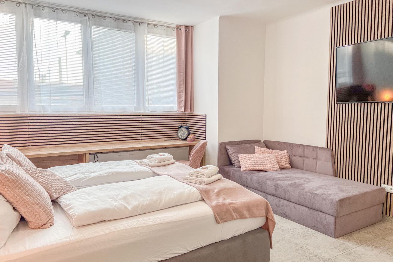 Een slaapkamer met een bed, een bank, een aan de muur bevestigde televisie en een raam met gordijnen.