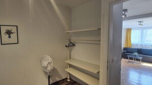 A room with a white fan, a framed picture on the wall, and a doorway leading to a living area with a sofa and a table.