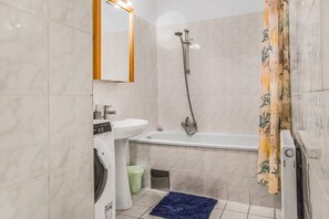 Une salle de bain équipée d’un lave-linge, d’un lavabo, d’une baignoire et d’une douche.