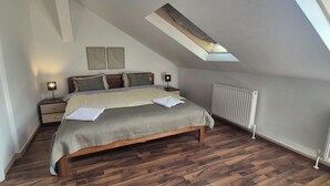 A bedroom with a sloped ceiling, a bed with a wooden frame, a radiator, and a skylight.