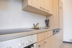 A kitchen with a stove, sink, and wooden cabinets.