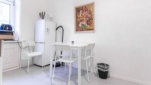 Eine kleine Küchenzeile mit einem weißen Kühlschrank, einem weißen Spülbecken und einem weißen Esstisch mit vier Stühlen.