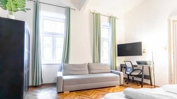 Ein Zimmer mit einer Couch, einem Schreibtisch mit Stuhl, einem Fernseher und einem Bett.
