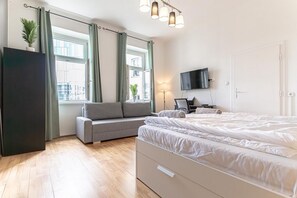 Ein Schlafzimmer mit Bett, einer Couch, einem Fernseher, einer Lampe und einem Fenster mit Vorhängen.