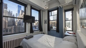 Een hotelkamer met een groot bed, een aan de muur bevestigde televisie en een stadszicht door grote ramen.