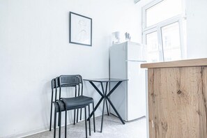 A small kitchenette with a refrigerator, a chair, a table, and a wooden counter.