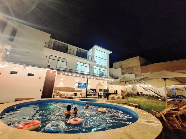 Una piscina con flotadores, una zona de estar cubierta y un edificio con múltiples ventanas y balcones.