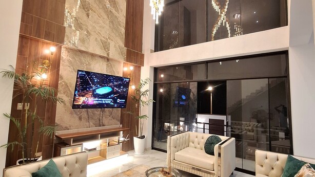 A modern living room with a large flat-screen TV, two sofas, a coffee table, and a decorative light fixture.