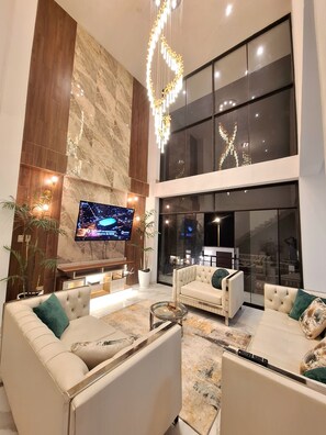 Una sala moderna con un televisor de pantalla plana grande, dos sofás, una mesa de centro y una lámpara decorativa.