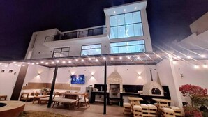 A modern two-story building with a covered patio area featuring outdoor seating and a barbecue grill.