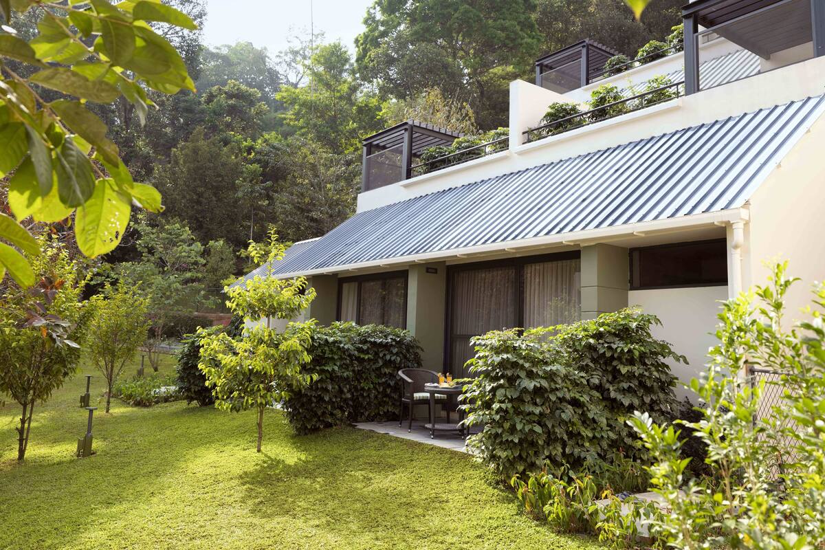 Une maison moderne avec un toit en pente, entourée d’un jardin bien entretenu et d’arbres.