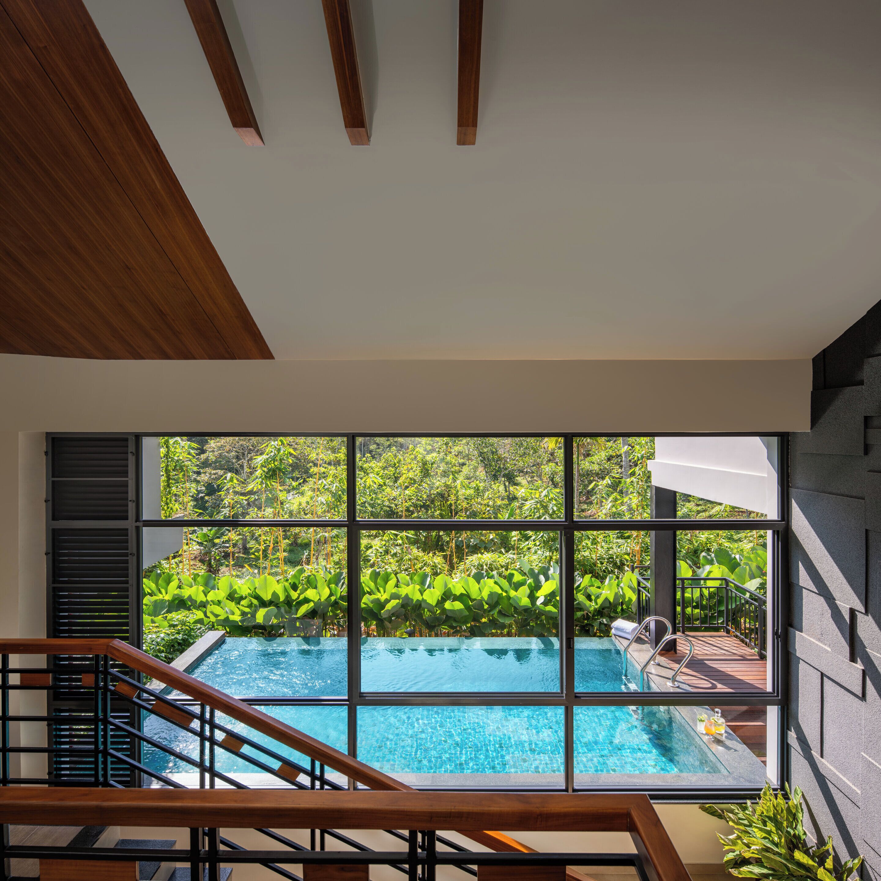 A modern interior with a large window overlooking a swimming pool and lush greenery.