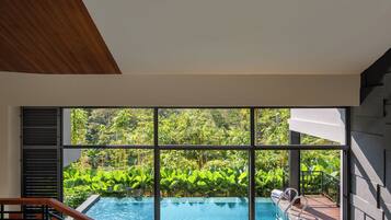 A modern interior with a large window overlooking a swimming pool and lush greenery.