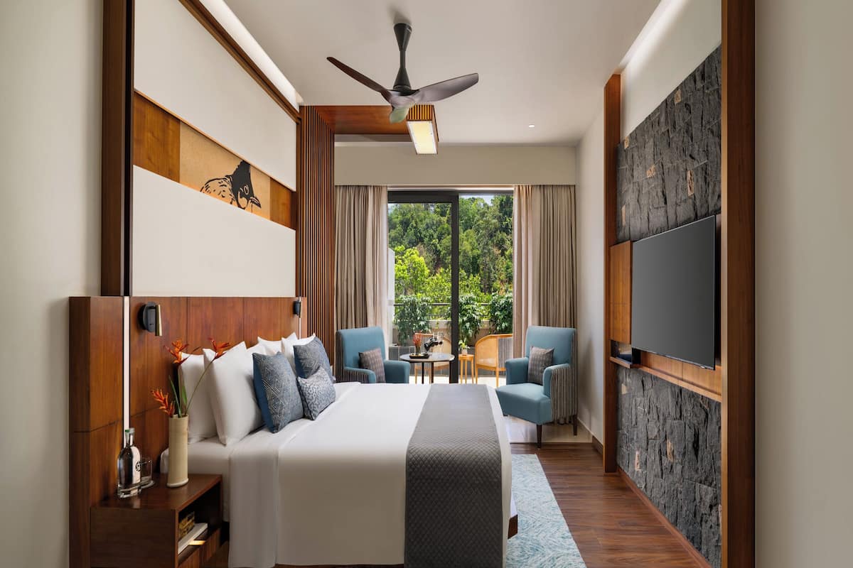 Une chambre d’hôtel moderne dotée d’un grand lit, d’un ventilateur de plafond, d’un téléviseur fixé au mur et offrant une vue sur l’extérieur par la fenêtre.