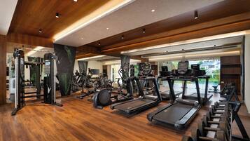 A spacious gym with various exercise equipment, wooden flooring, and a large mirror reflecting the space.