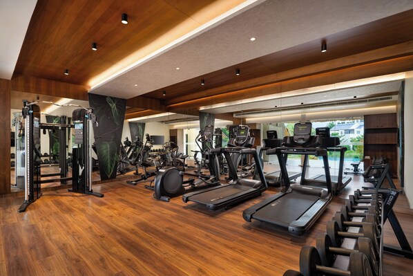 A spacious gym with various exercise equipment, wooden flooring, and a large mirror reflecting the space. - Scenic, Munnar - IHCL SeleQtions (Devikolam)