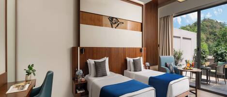 A hotel room with two beds, a desk with a chair, a ceiling fan, and a view of greenery outside.