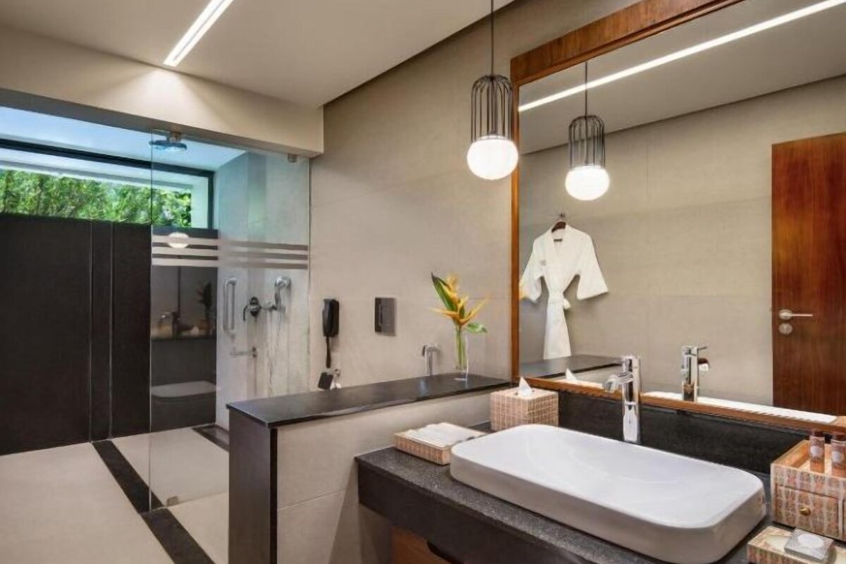 Een moderne badkamer met een grote spiegel, een witte wastafel en een houten wastafelmeubel.