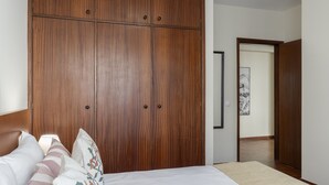 Un dormitorio con un armario de madera grande, una cama con almohadillas estampadas y un cuadro en la pared.
