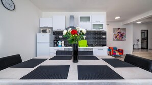 A modern kitchen with white cabinets, a black backsplash, and a dining area with a table set for four. - Awesome home in Sveti Lovrec Labinski (Sveti Lovrec Labinski)