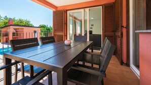 A balcony with a wooden table and chairs, a small vase, and a view of a swimming pool and building. - Awesome home in Sveti Lovrec Labinski (Sveti Lovrec Labinski)
