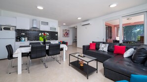 A modern living room with a black leather sofa, a dining table with chairs, and a kitchen area with white cabinets and black tiles. - Awesome home in Sveti Lovrec Labinski (Sveti Lovrec Labinski)