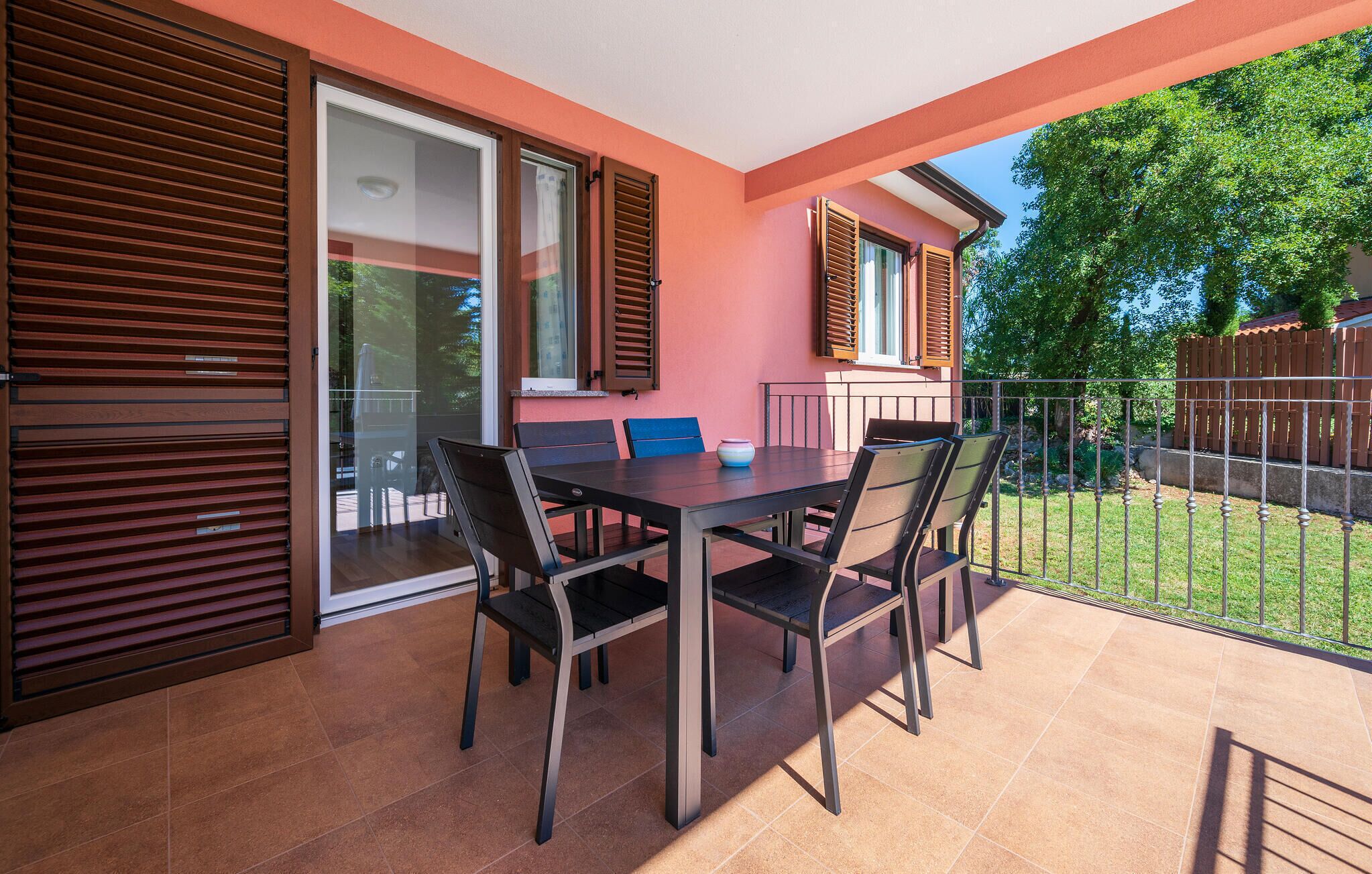 A patio with a table and chairs, a sliding glass door, and a view of a garden and house.