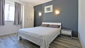 A bedroom with a bed, a nightstand, a wardrobe, a window with curtains, and wall-mounted lights. - Holiday apartment with a/c (Fažana)