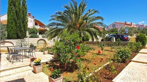 A courtyard with a palm tree, potted plants, a stone bench, and a stone wall.