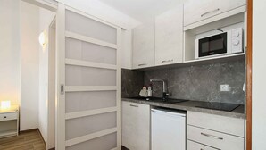 A compact kitchen with white cabinets, a microwave, a dishwasher, and a marble countertop.