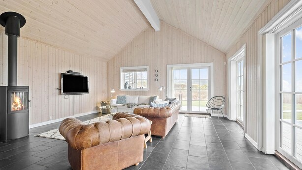 A spacious living room with a fireplace, leather sofas, a television, and large windows offering a view of the outdoors.