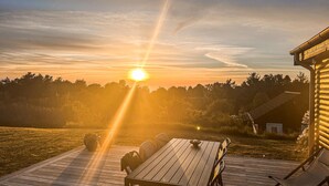 A wooden deck with a table and chairs, overlooking a forested area during sunset.