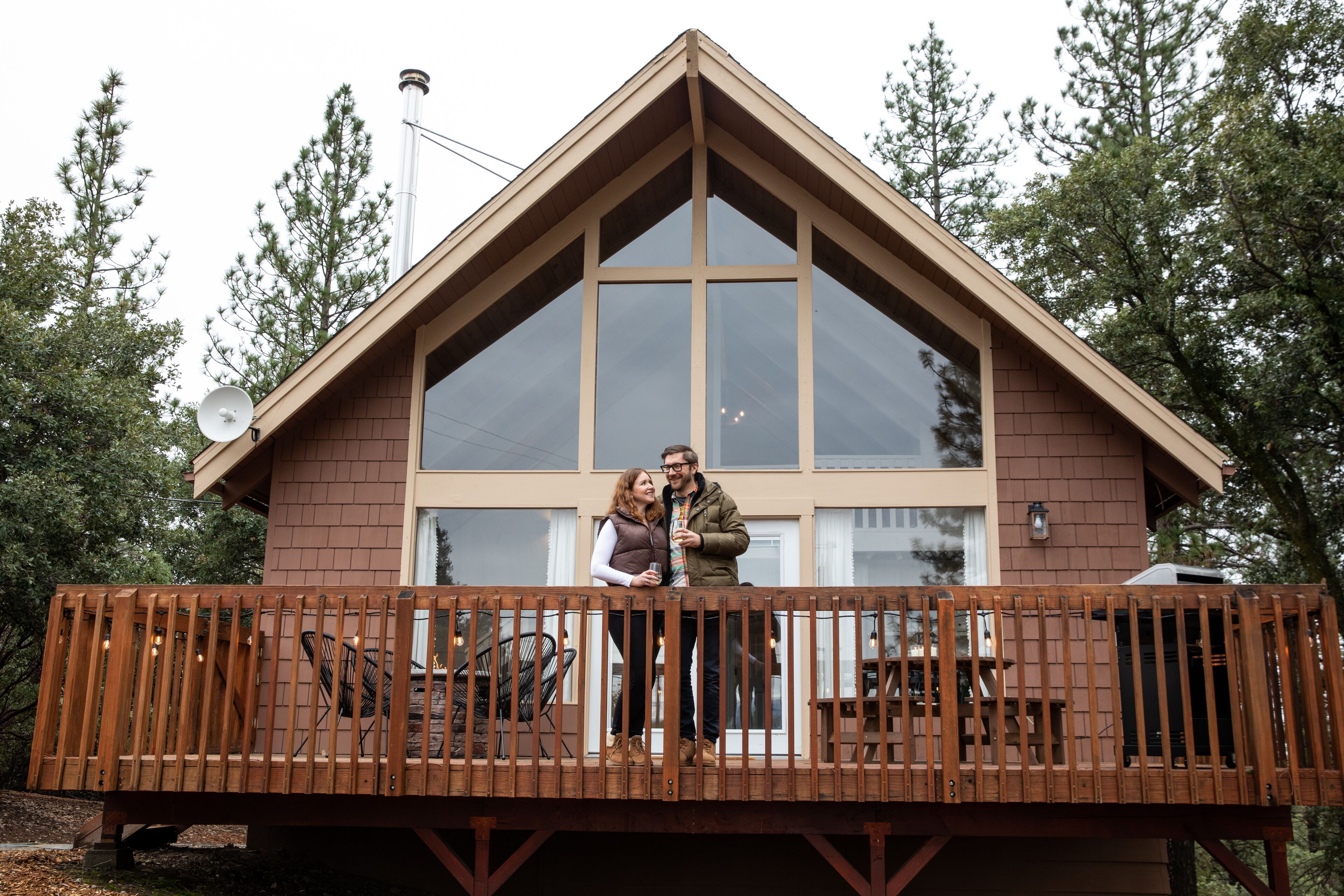 A wooden deck with a railing, a large window, and a view of trees.