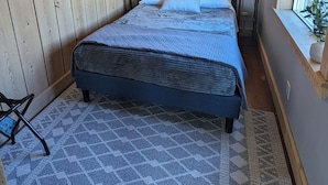A bedroom with a bed, two bedside lamps, a window with blinds, and a patterned rug.