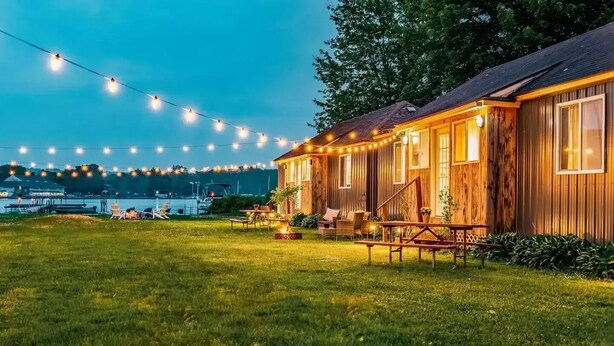 A wooden cabin with a deck, string lights, and a view of the water.