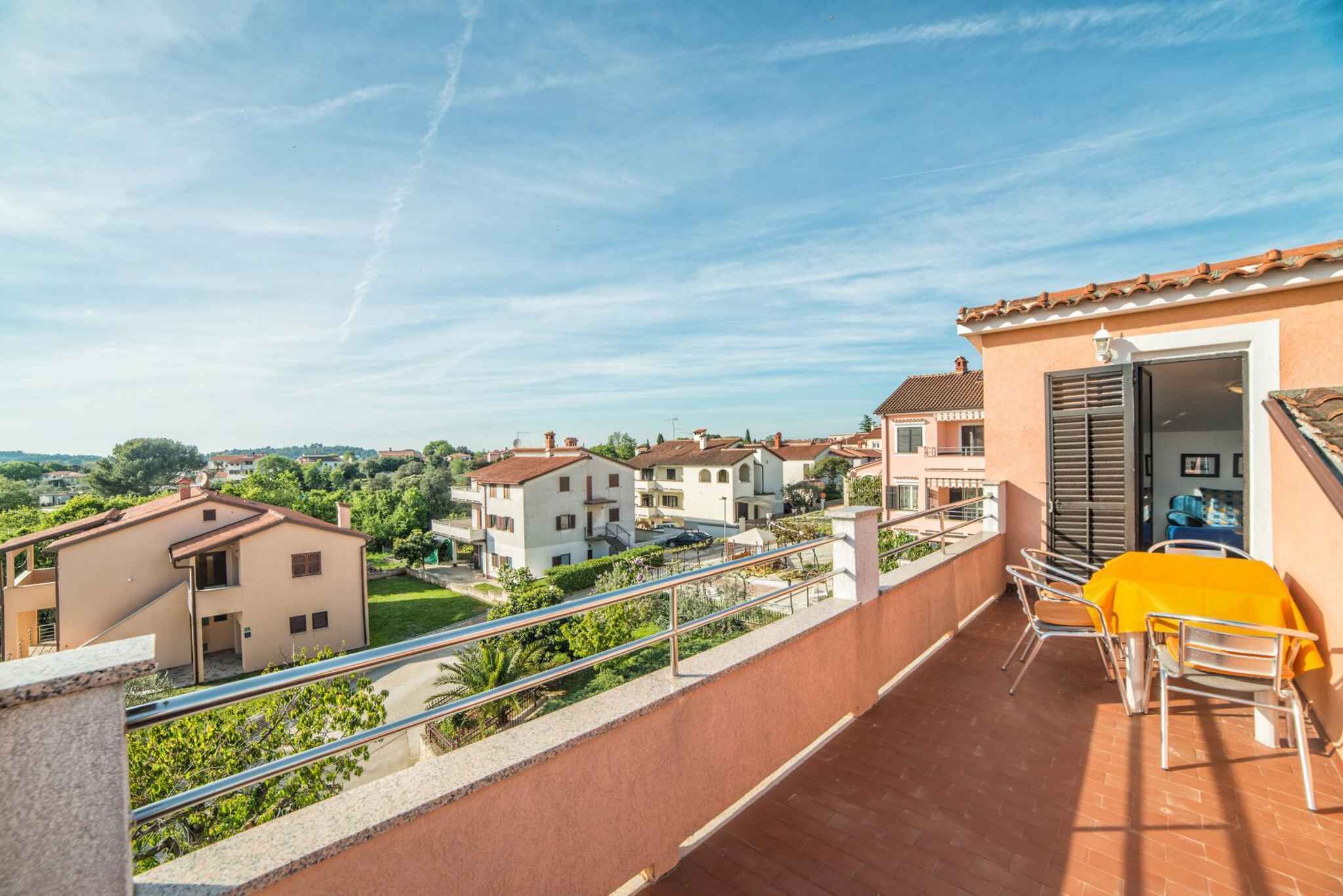 A balcony with a table and chairs, overlooking a residential area with houses and greenery.