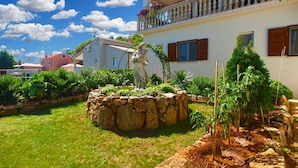 Un edificio blanco con una fuente de piedra, abundante vegetación y un cielo azul despejado.
