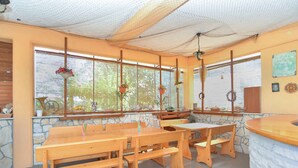 Un comedor con bancos y mesas de madera, paredes de piedra y cestas de flores colgantes.