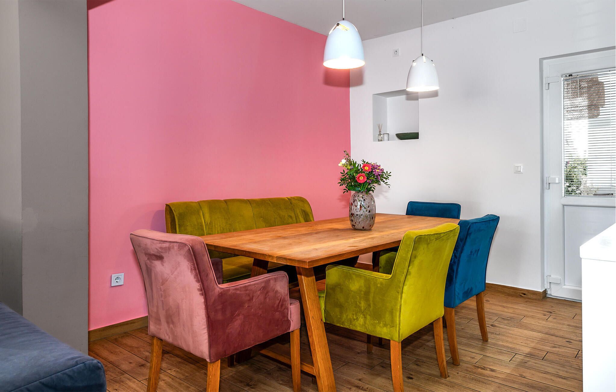 A dining area with a wooden table, colorful chairs, and a vase of flowers.