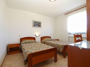 A small bedroom with two wooden beds, a nightstand, a table, and a chair.