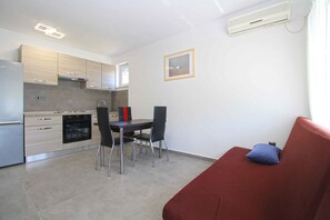 Cocina compacta con electrodomésticos modernos, comedor con sillas y sofá rojo con un cojín.