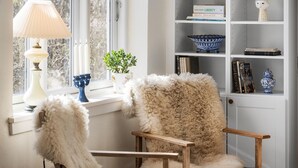 A cozy room with a window, a lamp, a bookshelf, and a fluffy chair.
