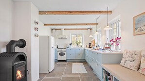 A modern kitchen with a wood-burning stove, a built-in oven, and a dining area with a bench and books.