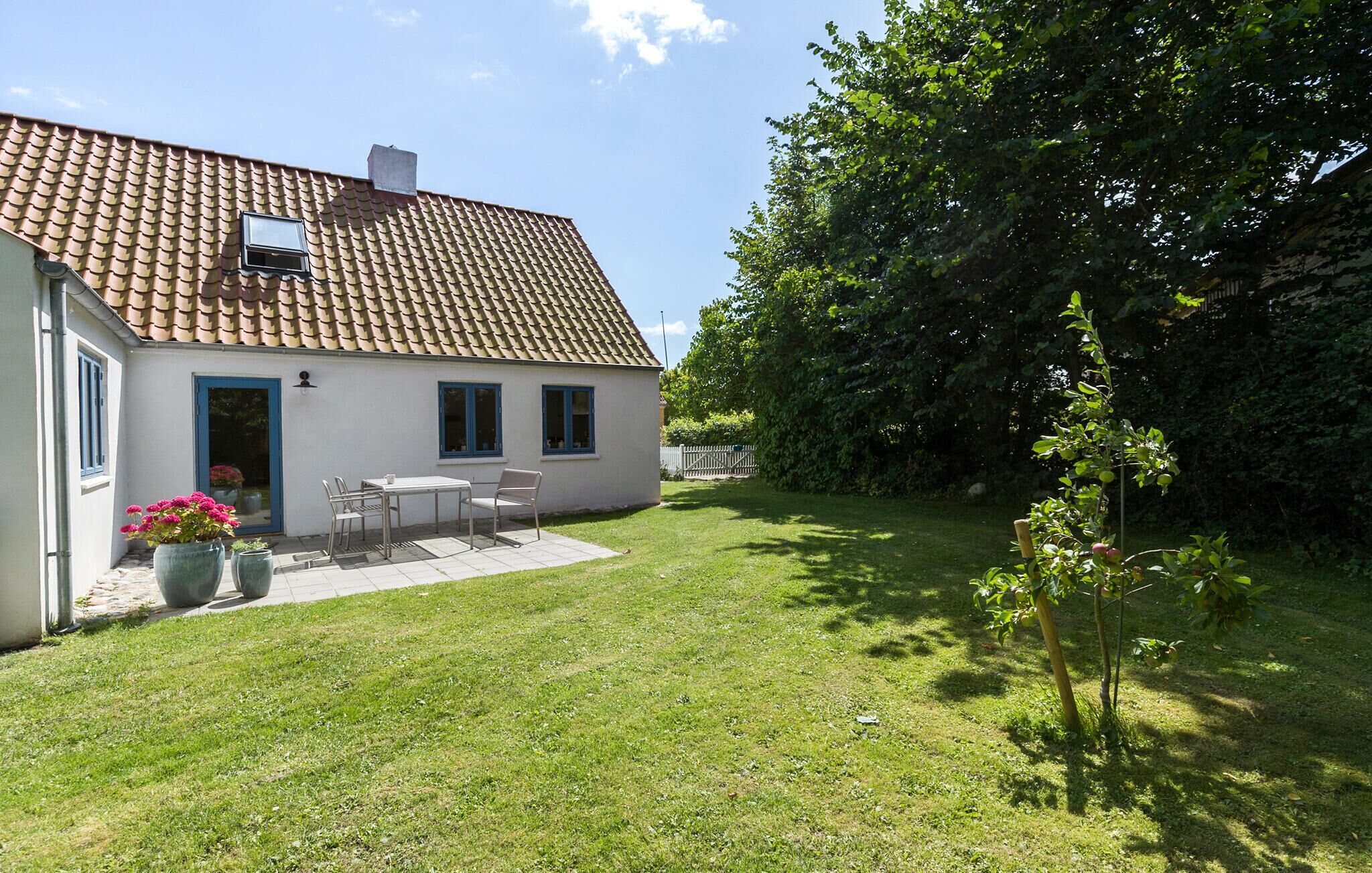 Ein Haus mit einem Ziegeldach, einer kleinen Terrasse mit Tisch und Stühlen und einem gepflegten Rasen.