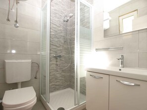 Een moderne badkamer met een glazen douchecabine, een toilet en een wastafel met spiegel.