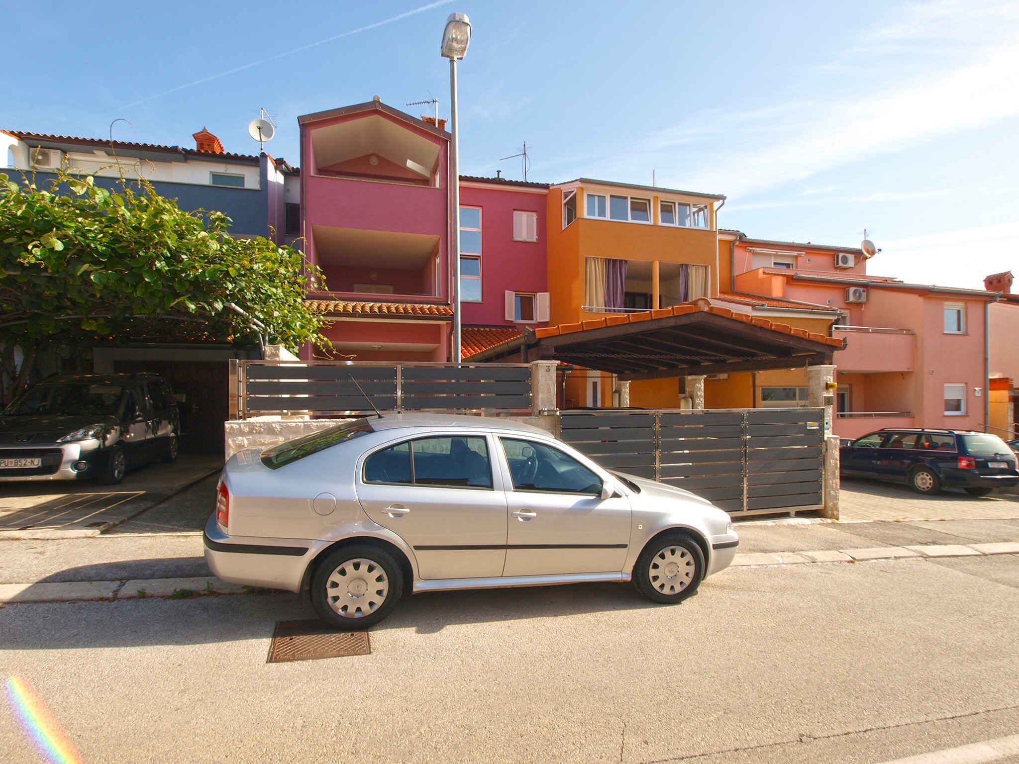 A beige sedan parked on a residential street with colorful houses in the background.