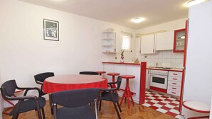 Eine kompakte Küche mit rotem und weißem Farbdesign, einem Fischgrätparkettboden und grundlegender Ausstattung, darunter ein Tisch, Stühle und ein kleiner Backofen.