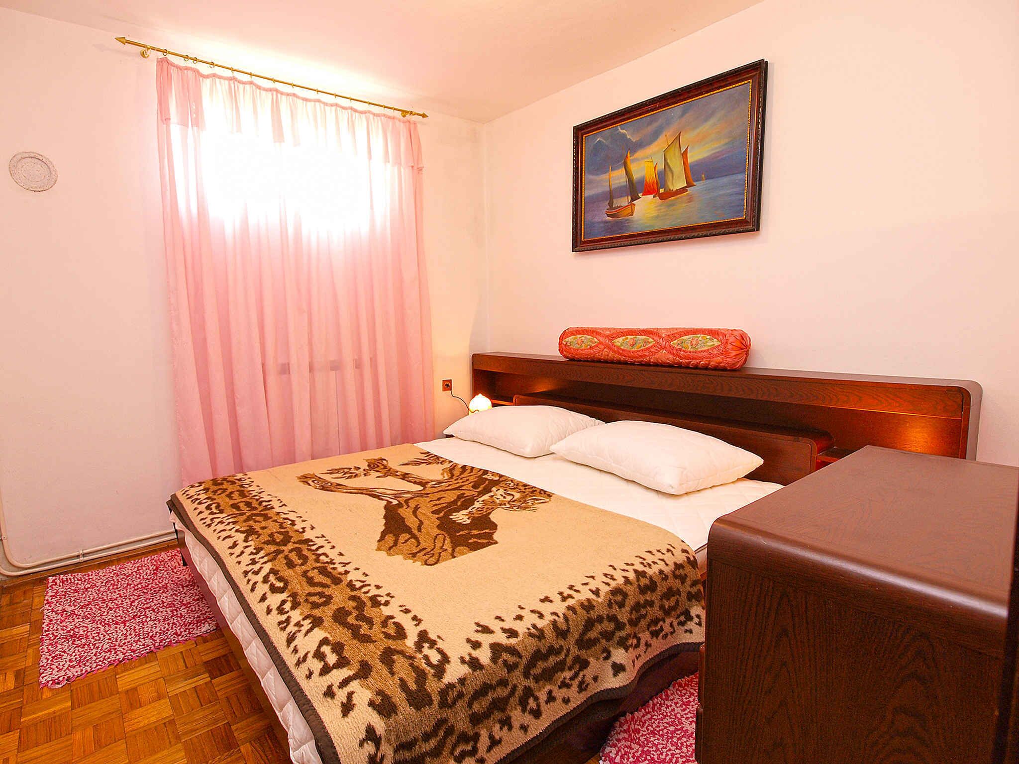 A bedroom with a bed, a wooden headboard, a painting, and a red cushion.