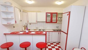 Eine kleine Küche mit weißen Schränken, roten Akzenten, einem Schachbrettboden und einer Bar mit Hockern.